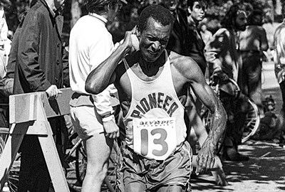 Ted Corbitt running and grimacing Olympic Airways bib